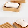 A set of natural bamboo soap dishes holding pink and white bar soaps.