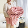A person is holding a large, fluffy pink fleece blanket with textured ridges in front of a white sofa.