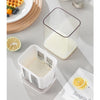 A clear stainless steel yogurt strainer with a fine mesh filter is shown next to a glass of milk and an orange slice.