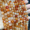 A hand holds a string of square faceted natural stone beads in shades of amber, orange, and pink.