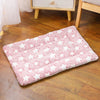 A pink and white plush pet sleeping mat is laid on a wooden floor next to a light-colored furniture piece.