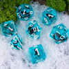 A set of translucent blue resin dice scattered on white snow next to green moss.