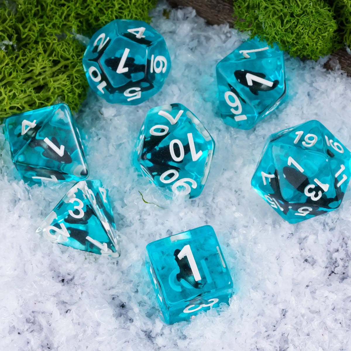 A set of translucent blue resin dice scattered on white snow next to green moss.