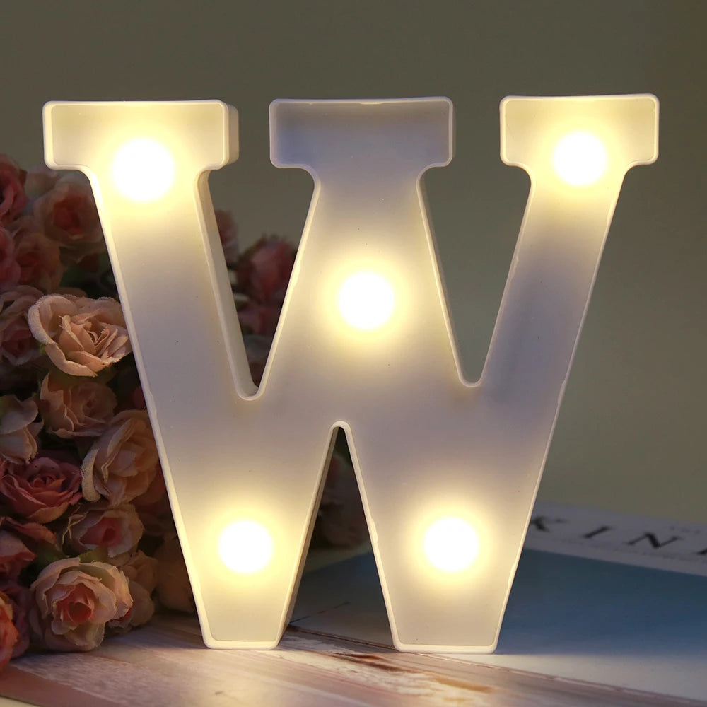 Lumière de nuit alphabétique blanche LED formant la lettre W, posée sur une surface en bois à côté de roses roses.