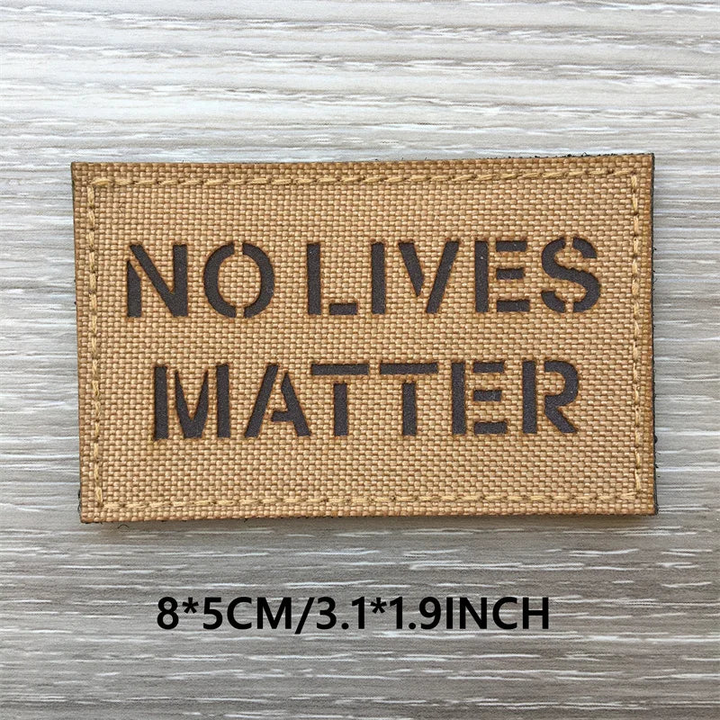 A rectangular tan woven patch with black text reading NO LIVES MATTER on a weathered wooden surface.