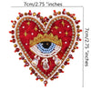 A heart-shaped patch embroidered with red fabric, gold and blue rhinestones, and a central eye design.