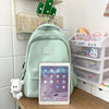 A light green waterproof nylon laptop backpack resting on a wooden surface next to an iPad and clear storage trays.