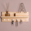 A wooden shelf holds transparent push pins and a metal triangle rack on a beige wall.