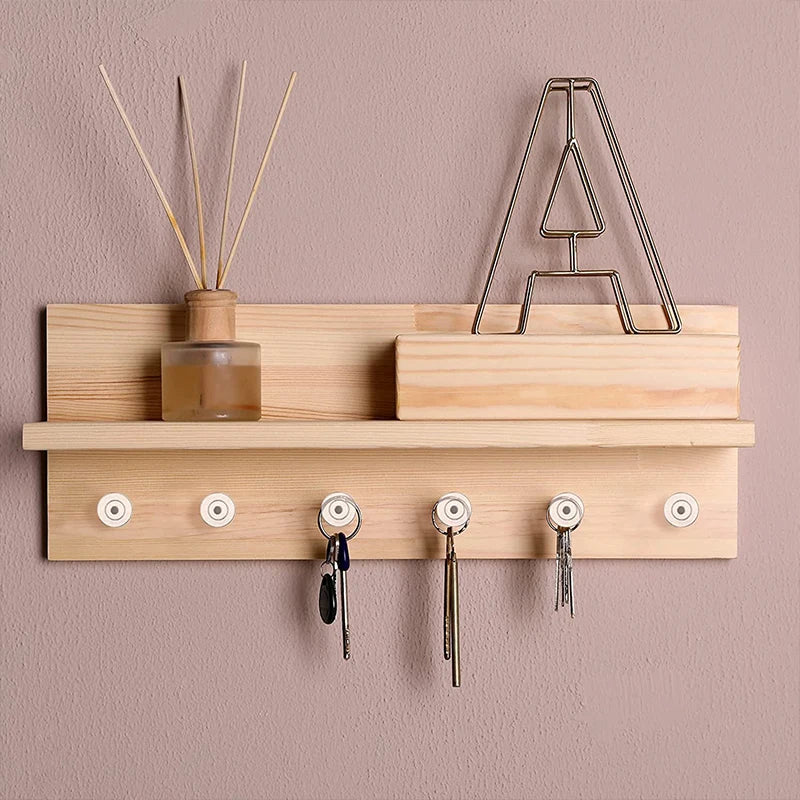 A wooden shelf holds transparent push pins and a metal triangle rack on a beige wall.