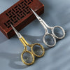 Pair of vintage stainless steel sewing scissors with chain resting on a dark wooden box.