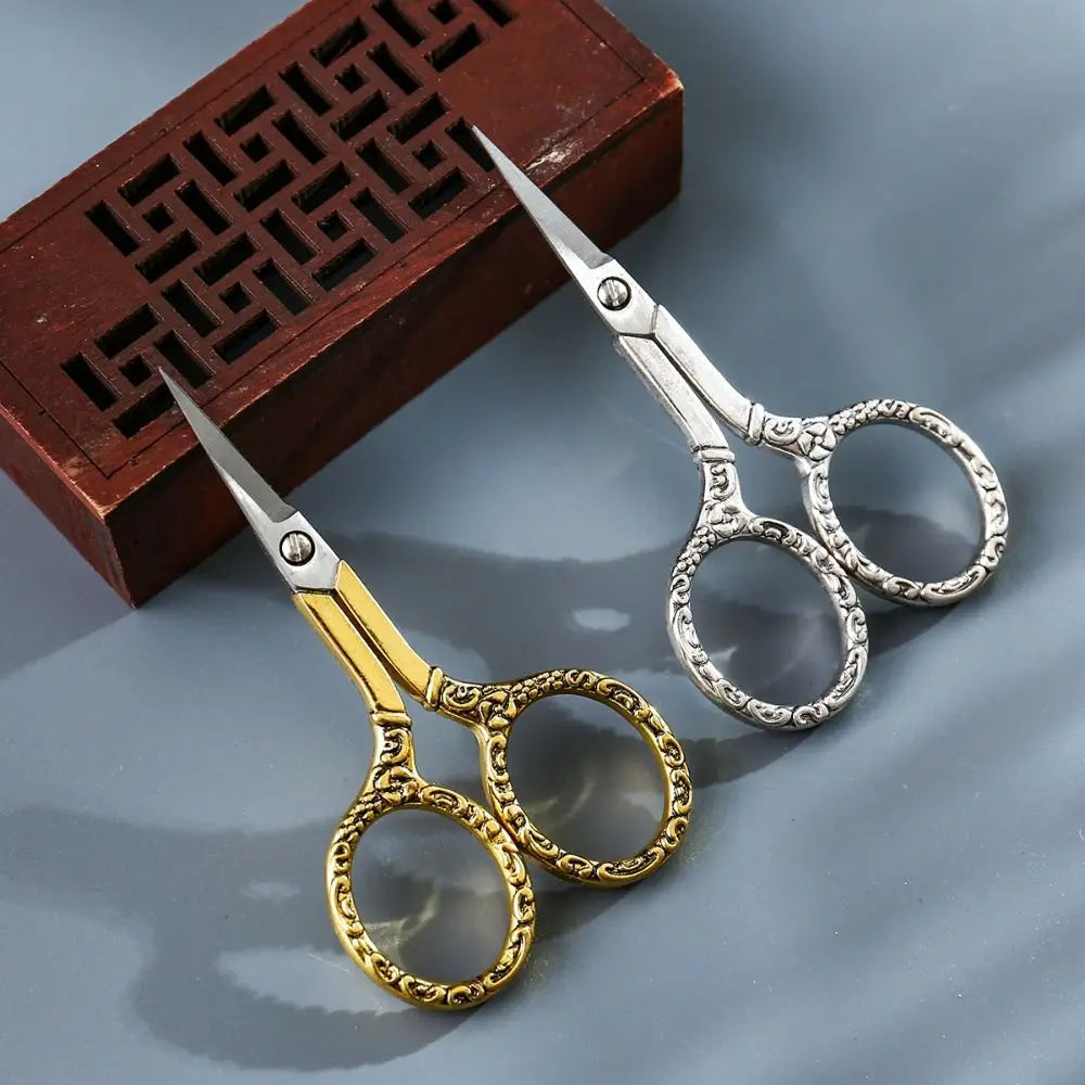 Pair of vintage stainless steel sewing scissors with chain resting on a dark wooden box.