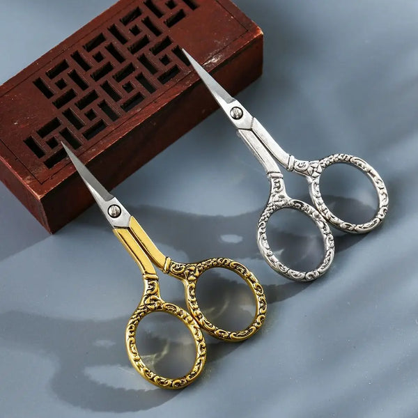 Pair of vintage stainless steel sewing scissors with chain resting on a dark wooden box.