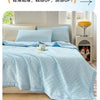 Light blue waffle-weave quilt folded on a bed with white pillows and a yellow lamp.
