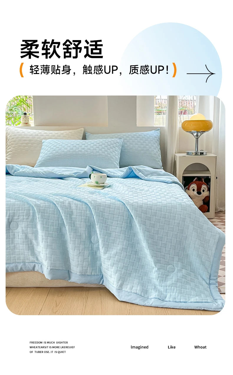 Light blue waffle-weave quilt folded on a bed with white pillows and a yellow lamp.