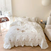 A white duvet cover set with pink rose embroidery and lace details displayed on a bed in a bright room.