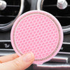 A pink crystal rhinestone non-slip cup mat is being held over a car's cup holder.