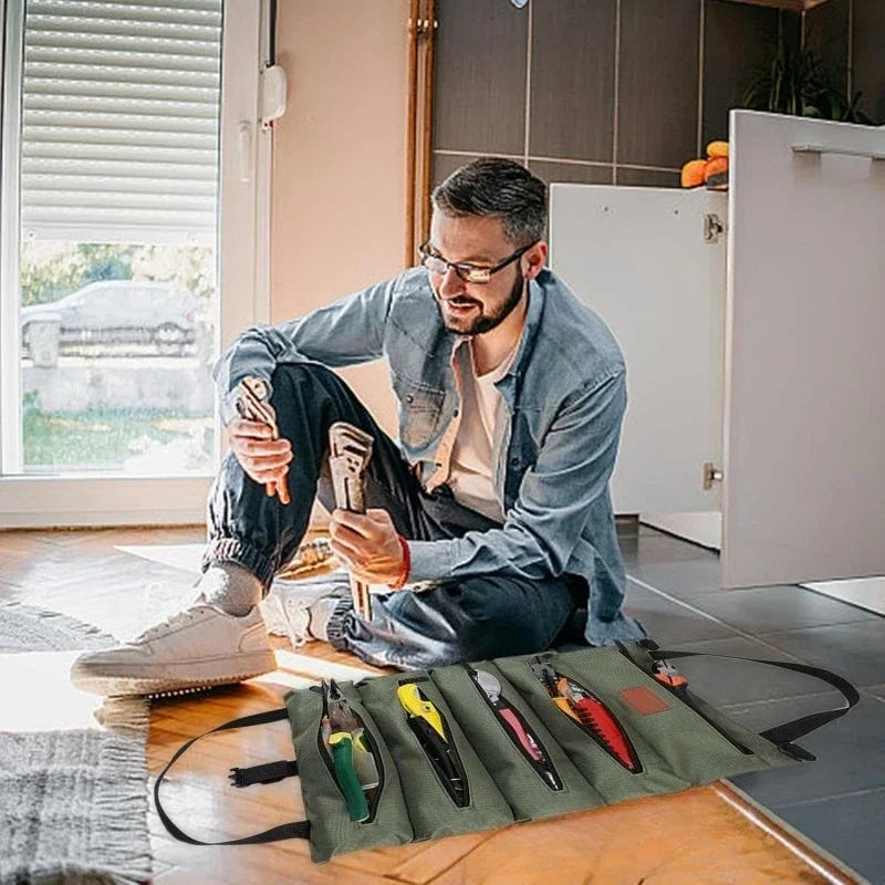 A man is organizing various tools in a green roll-up multi-pocket organizer bag on a wooden table.