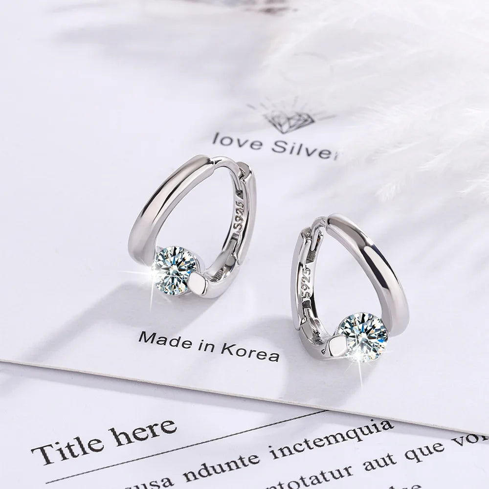 Silver hoop earrings featuring a clear stone set in a delicate design against a white background.