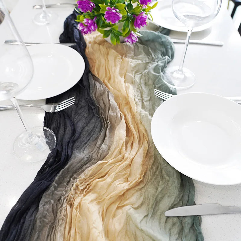 A cotton gauze table runner featuring a rustic country boho design with shades of black, beige, and sage green on a white tab