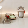 A clear glass portable travel soap box with a drainage lid and an open container holding a green soap bar.