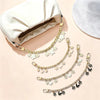 A gold chain necklace with white flowers and pearl charms draped next to a cream-colored clutch bag.