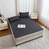 A gray waterproof mattress protector with elastic straps is displayed on a bed, next to a white chair and light-colored furni