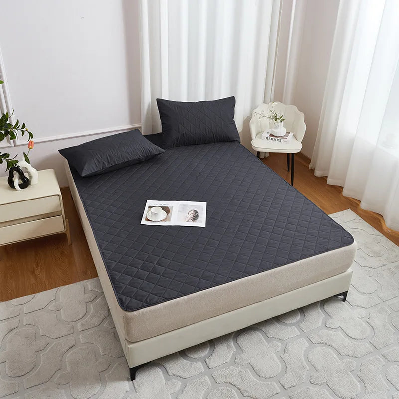 A gray waterproof mattress protector with elastic straps is displayed on a bed, next to a white chair and light-colored furni