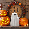 A white ghost resin statue stands in front of carved pumpkins and a wreath for Halloween decor.