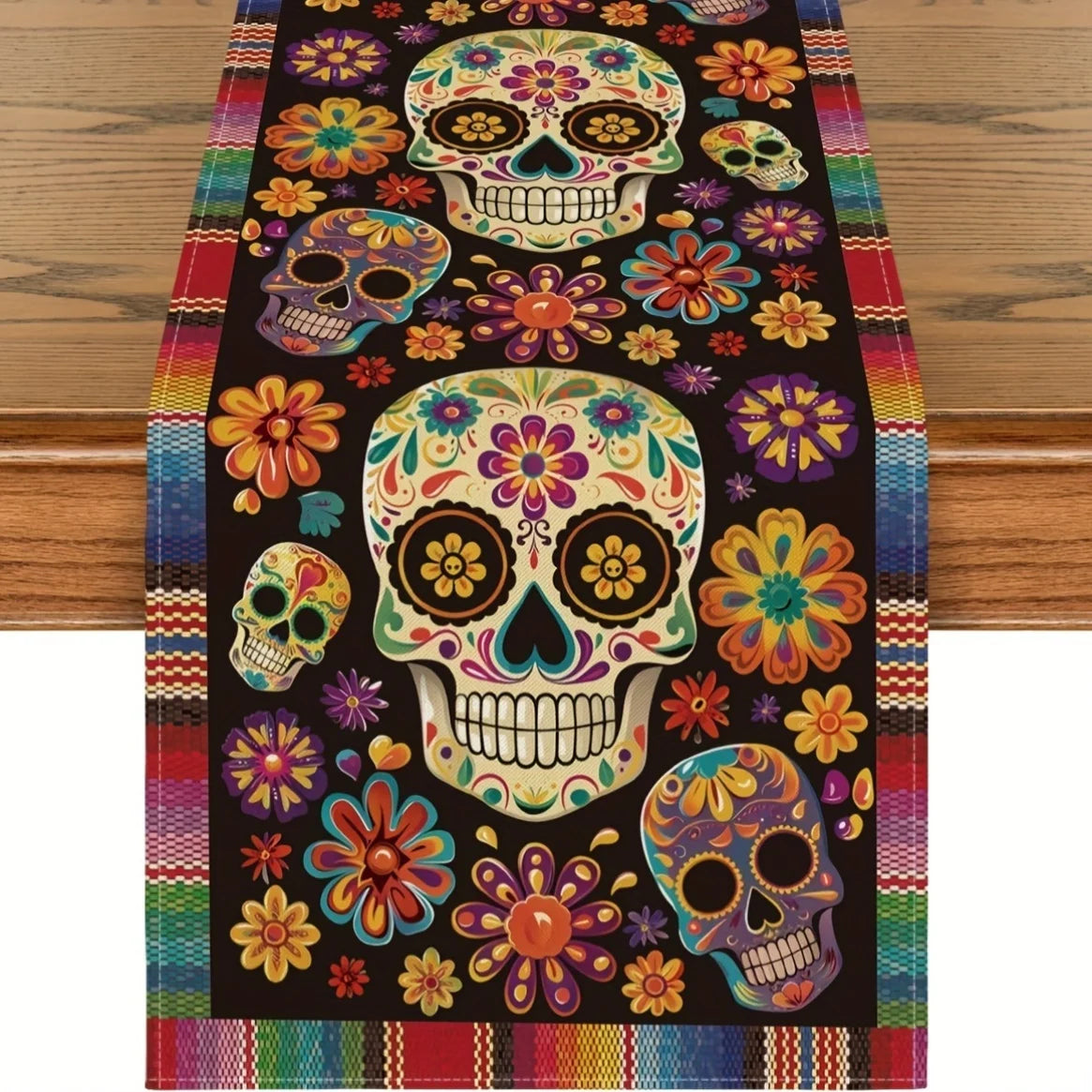 A colorful Day of the Dead table runner featuring skulls and floral designs on a dark background.