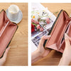A pink leather wallet with a gold trim is shown open, next to a cup and some floral elements.