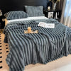 A thick, gray faux fur blanket is draped over a bed, featuring vertical pleats and used as bedding.