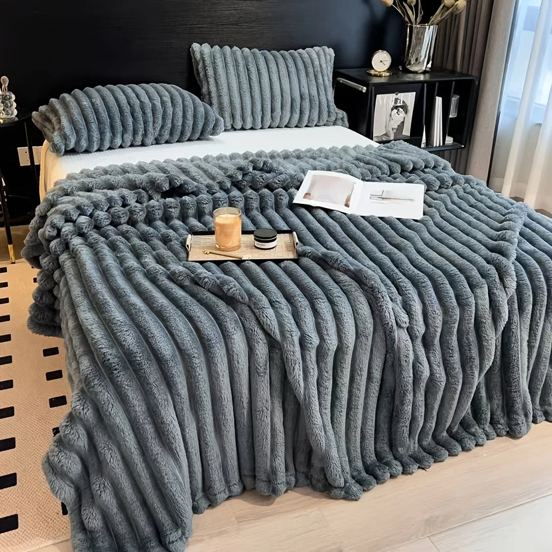 A thick, gray faux fur blanket is draped over a bed, featuring vertical pleats and used as bedding.