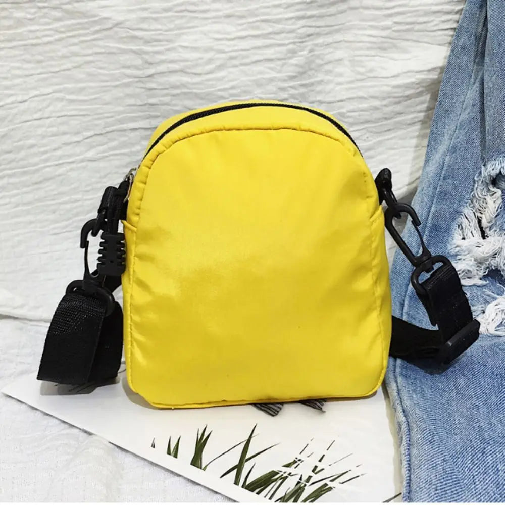 A bright yellow mini canvas crossbody bag with black straps resting on a white surface next to denim fabric.