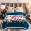 A teal weighted plush blanket with pink and yellow floral embroidery is displayed on a bed.