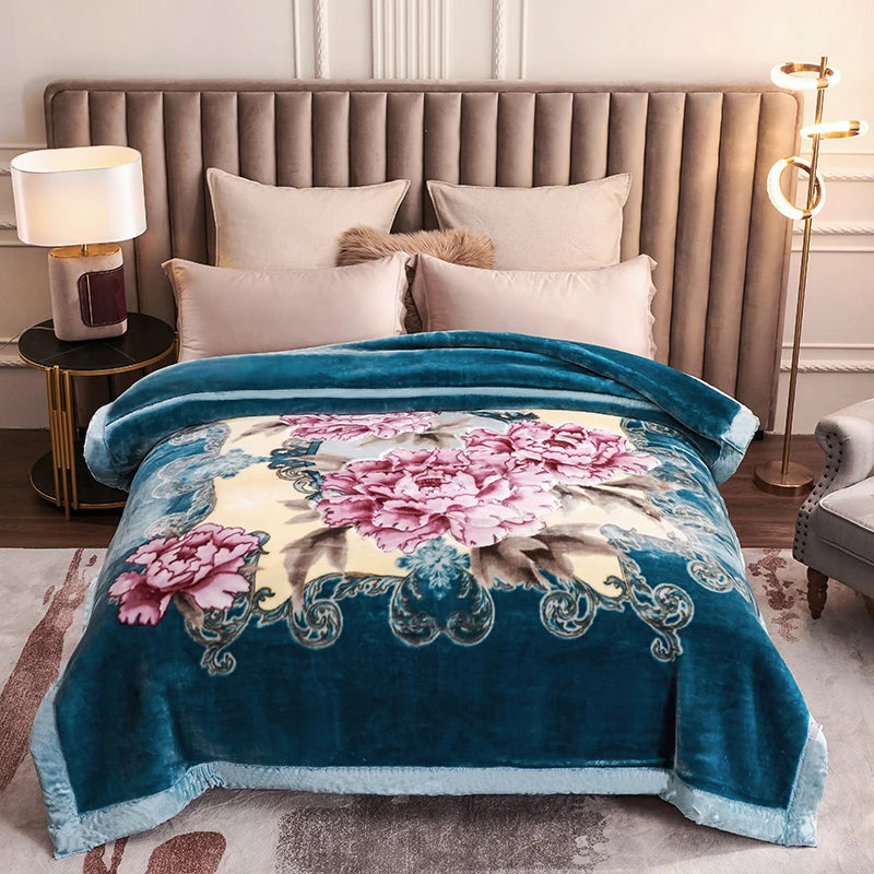 A teal weighted plush blanket with pink and yellow floral embroidery is displayed on a bed.