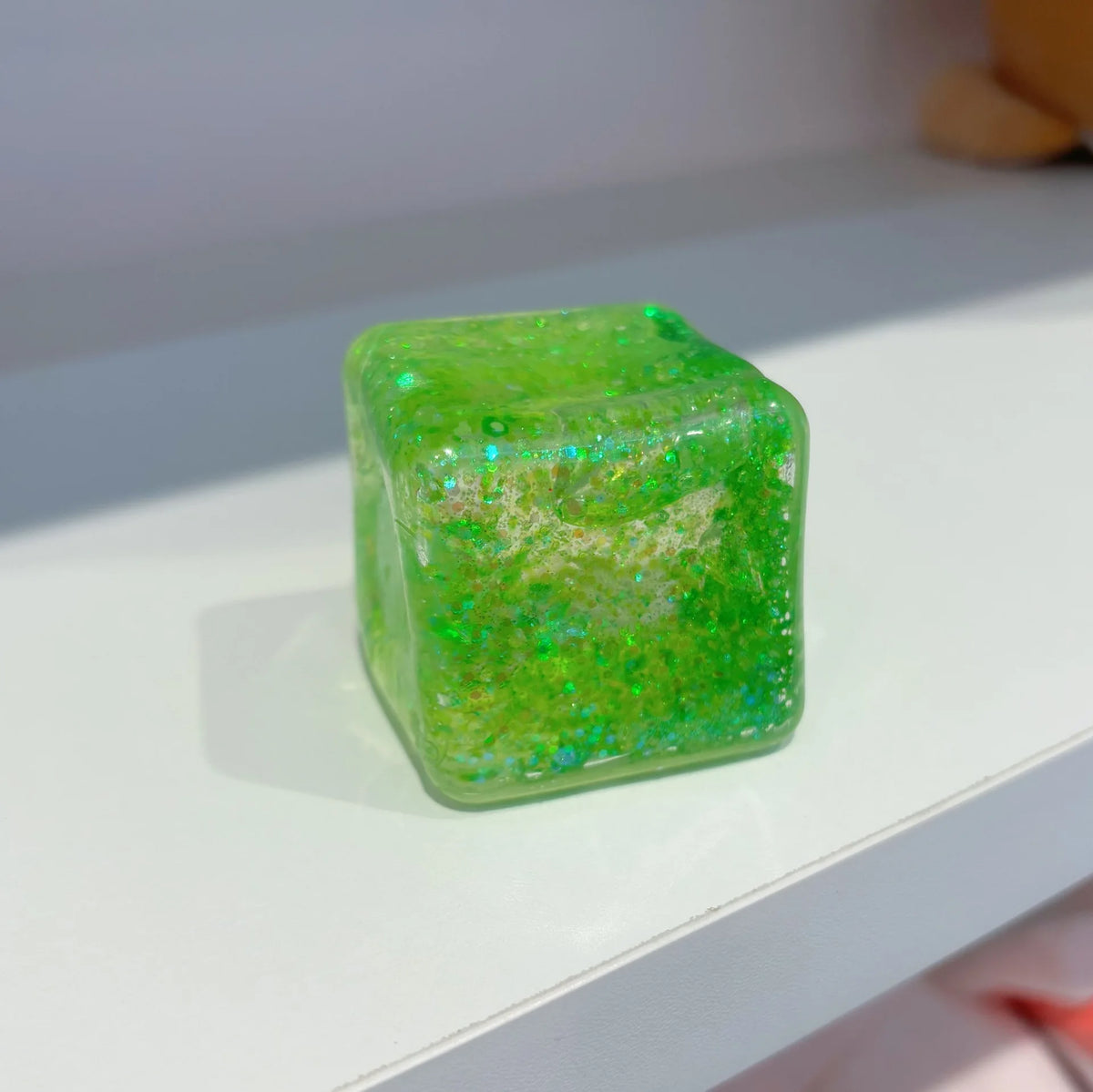 Ein quadratisches, durchsichtiges limettengrünes Fidget-Squishy-Spielzeug auf einer weißen Oberfläche.