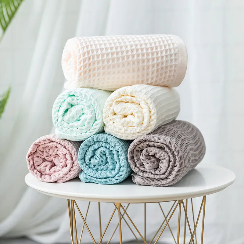A stack of fluffy, light pink and white waffle weave bath towels on a gold stand.