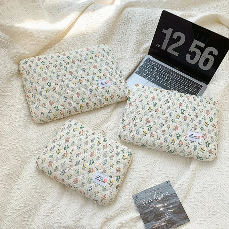 A beige floral printed laptop sleeve is shown next to an open black laptop and a dark gray card.
