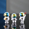Three handcrafted astronaut figurines in white and gold resin displayed on a reflective surface.