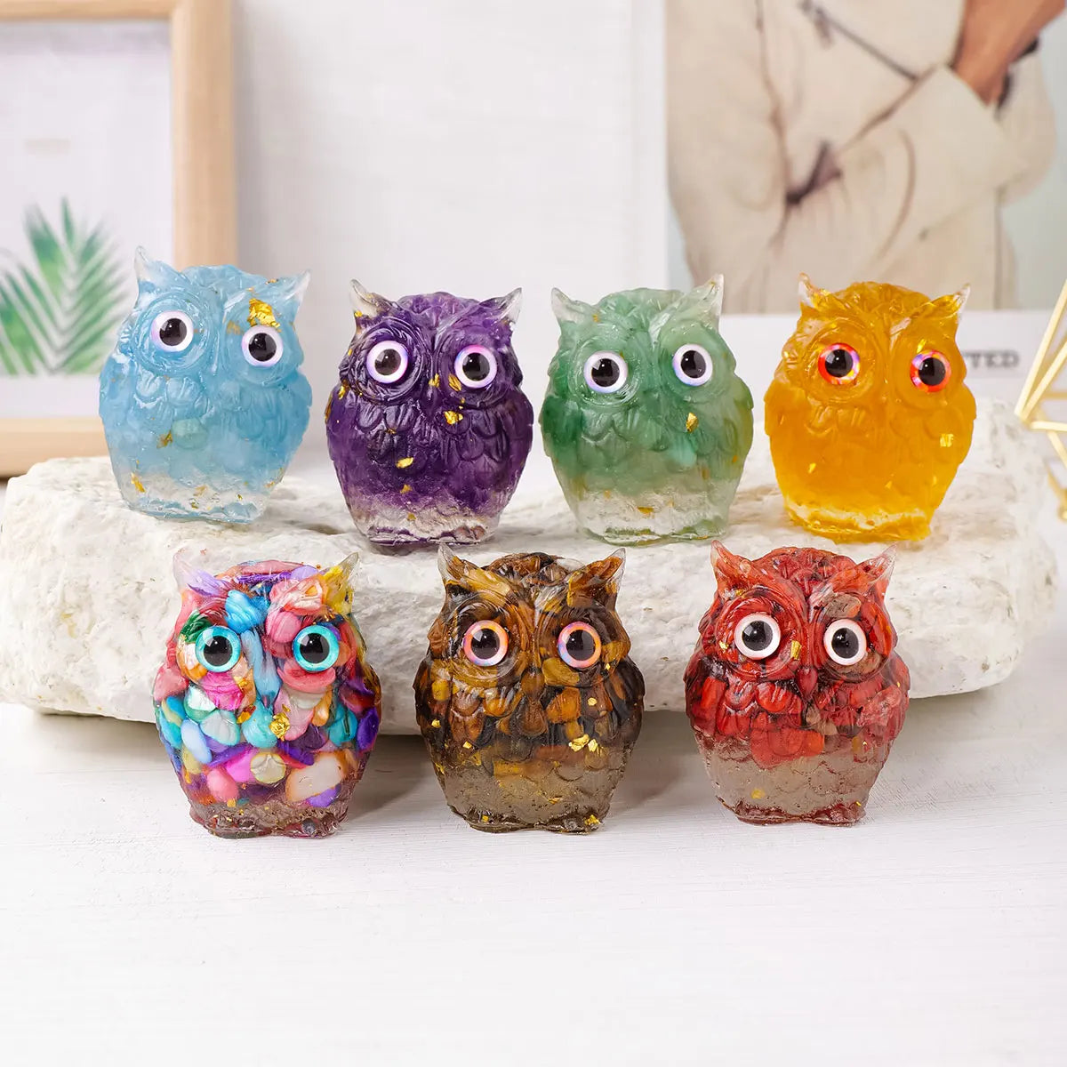 A collection of handcrafted crystal owl figurines in various colors and finishes displayed on a white surface.