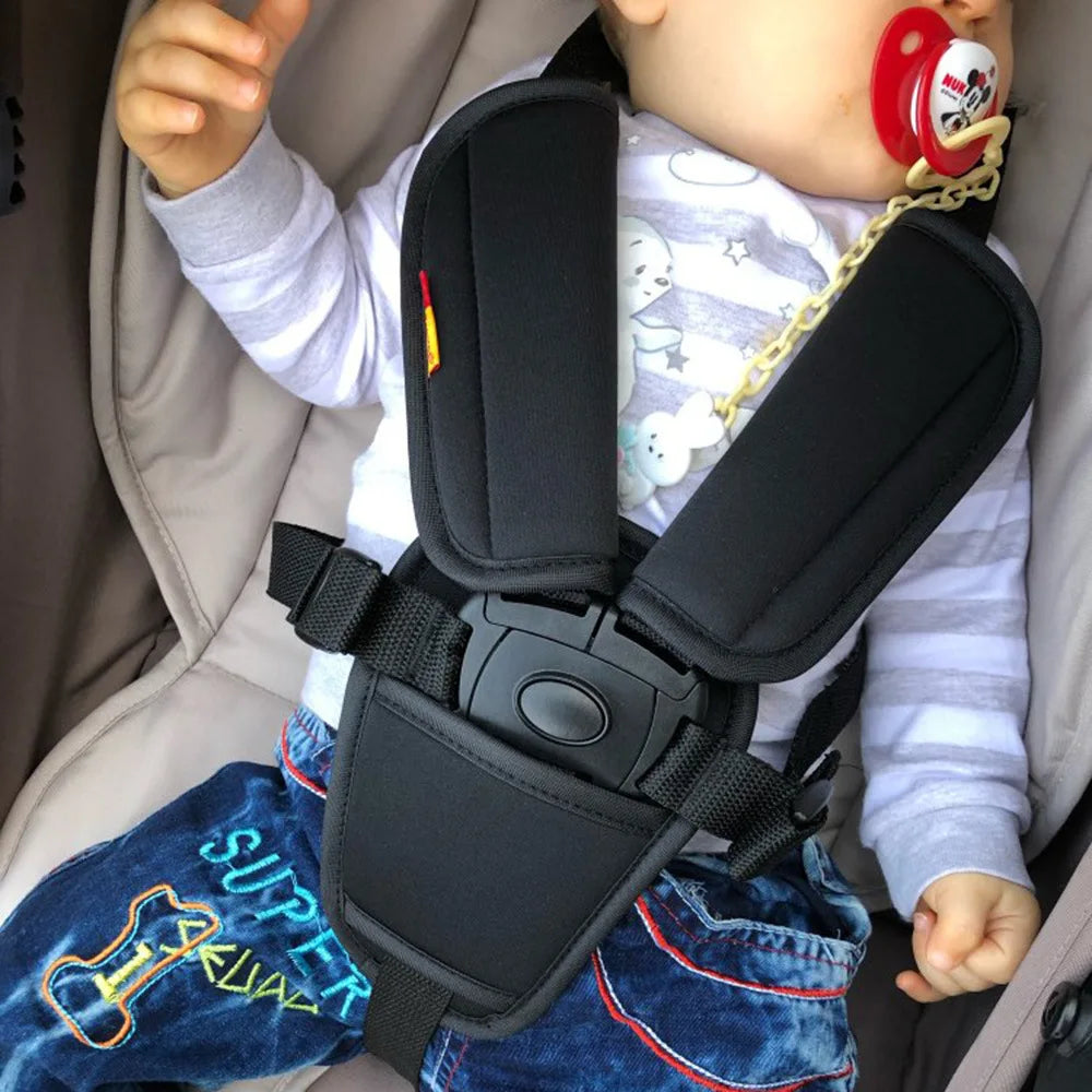A baby is wearing a black safety belt cushion cover designed for a stroller or car seat.
