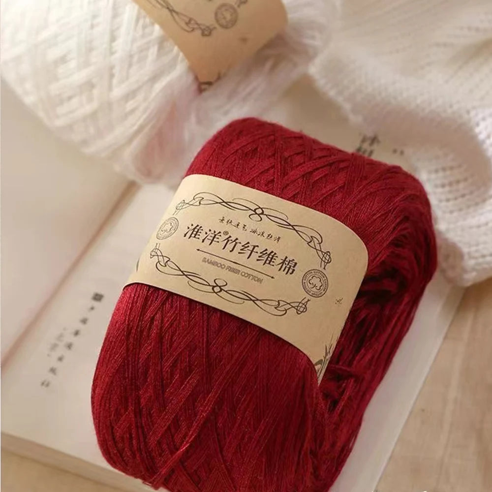A ball of deep red pure cotton yarn for knitting and crochet is shown next to a book.