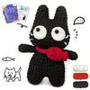 A black crocheted animal amigurumi featuring large eyes and a red accessory, with yarn and instructions nearby.