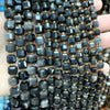 A hand holds a strand of natural stone square faceted beads in various shades of black and gray.