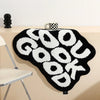 A black rug with white text spelling GOOD LOOK hanging on a light-colored wall.