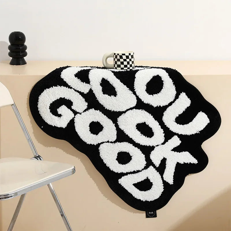 A black rug with white text spelling GOOD LOOK hanging on a light-colored wall.