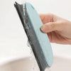 A hand is holding a light blue pet hair removal brush with water dripping from the bristles.