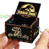 A hand holding a vintage hand-crank wooden music box with a Jurassic Park theme and an open lid.