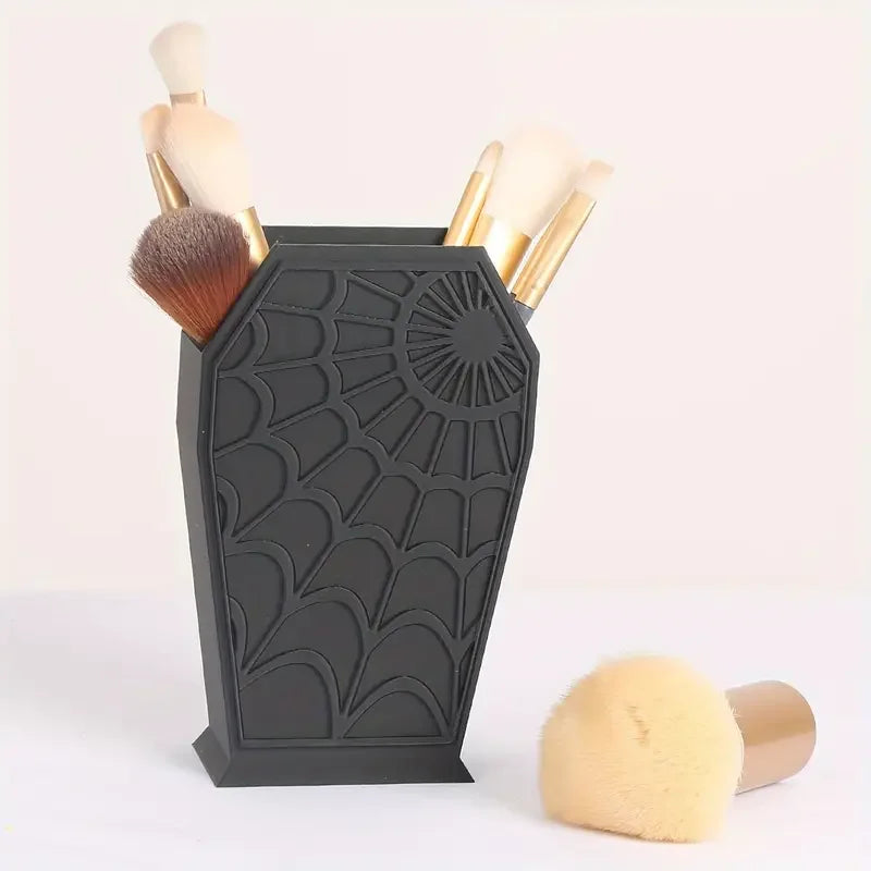 A black coffin-shaped makeup brush holder with a spider web design, holding several makeup brushes.