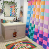 A colorful shower curtain display featuring vertical panels in rainbow plaid patterns and a rug with the text Hey Good Okin.